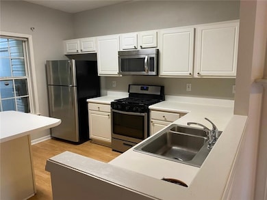 Kitchen with appliances with stainless steel finishes, light wood finished floors, white cabinets, and light countertops