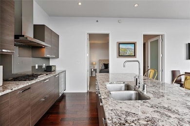 Kitchen featuring wall chimney range hood, a sink, stainless steel gas cooktop, dark wood finished floors, and modern cabinets