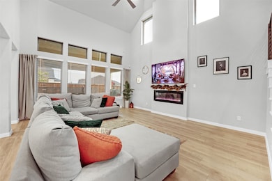 Living area with a high ceiling, a glass covered fireplace, ceiling fan, and light wood-type flooring