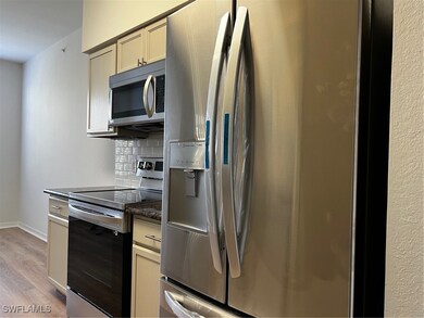 Kitchen with stainless steel refrigerator with ice dispenser, stove, light wood finished floors, backsplash, and baseboards