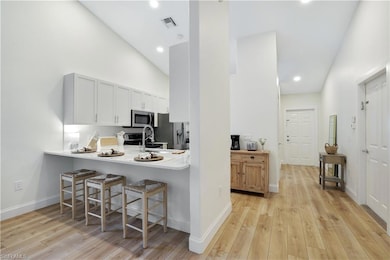Kitchen with appliances with stainless steel finishes, high vaulted ceiling, a breakfast bar area, light wood-type flooring, and a sink
