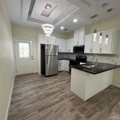 Kitchen featuring appliances with stainless steel finishes, a raised ceiling, a peninsula, dark countertops, and recessed lighting