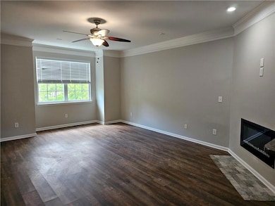 Unfurnished living room with ornamental molding, dark wood-style flooring, ceiling fan, a fireplace with flush hearth, and baseboards