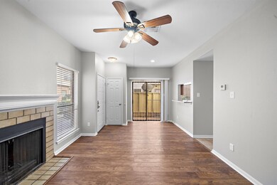 This inviting living space features hardwood floors, a cozy fireplace, and ample natural light from large windows. A ceiling fan provides comfort, and sliding doors lead to a private outdoor area. 