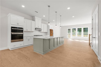 Kitchen with white cabinets, double oven, hanging light fixtures, a center island with sink, and decorative backsplash