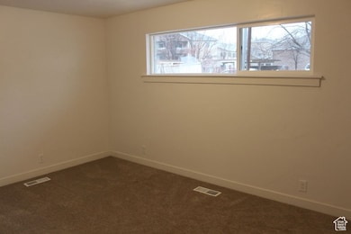 Spare room featuring dark colored carpet and baseboards