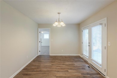 Unfurnished room with a notable chandelier, baseboards, visible vents, and dark wood-type flooring