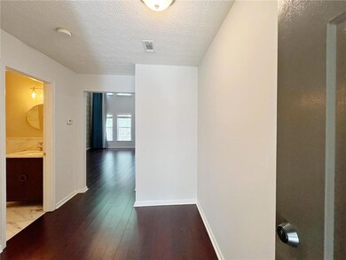 Hallway with a textured ceiling, visible vents, baseboards, a sink, and dark wood-style floors