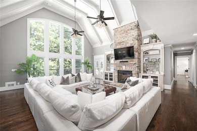 Living room featuring high vaulted ceiling, a stone fireplace, dark wood-type flooring, beamed ceiling, and a ceiling fan