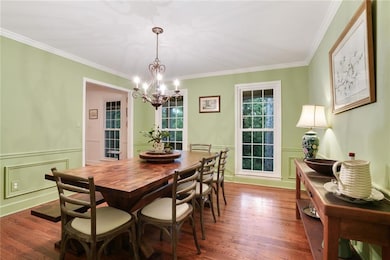 Dining room with a chandelier, wood finished floors, ornamental molding, and a wainscoted wall