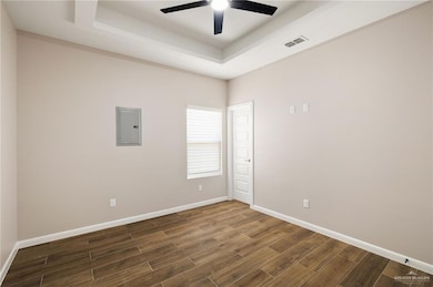 Unfurnished room with a raised ceiling, electric panel, dark wood-style flooring, and a ceiling fan