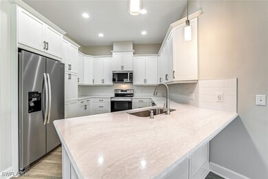 Kitchen with backsplash, stainless steel appliances, a peninsula, white cabinetry, and light stone counters