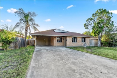 Single story home featuring solar panels, brick siding, a carport, concrete driveway, and a shingled roof
