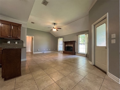 Unfurnished living room featuring crown molding, light tile patterned flooring, a fireplace with raised hearth, vaulted ceiling, and a ceiling fan