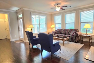 Living room, crown molding, ceiling fan, dark wood style finished floors, baseboards.