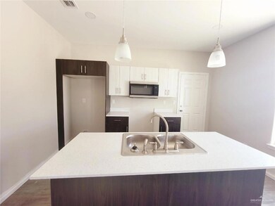 Kitchen featuring stainless steel microwave, a kitchen island with sink, white cabinetry, pendant lighting, and dark wood-style flooring