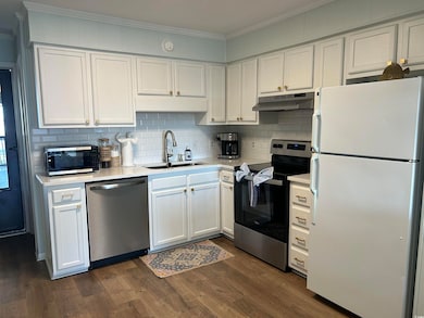 Kitchen featuring appliances with stainless steel finishes, white cabinetry, tasteful backsplash, ornamental molding, and under cabinet range hood