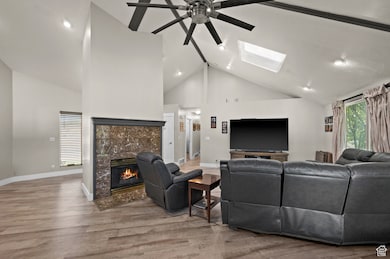 Living area featuring wood finished floors, a skylight, high vaulted ceiling, a tile fireplace, and ceiling fan
