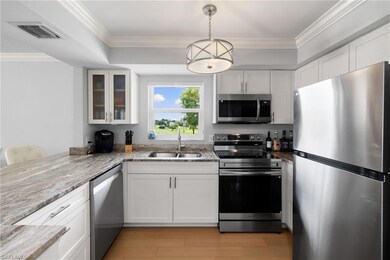 Kitchen with stainless steel appliances, white cabinetry, crown molding, glass insert cabinets, and decorative light fixtures