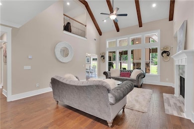Living room featuring ceiling fan, wood-type flooring, a premium fireplace, beamed ceiling, and high vaulted ceiling