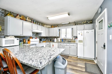 Kitchen with white appliances, a peninsula, under cabinet range hood, a sink, and a breakfast bar area