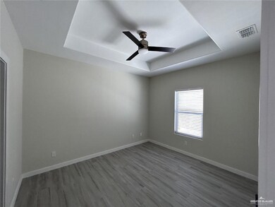 Unfurnished room with a tray ceiling, wood finished floors, a ceiling fan, and baseboards