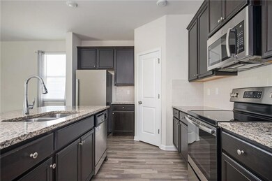 Kitchen featuring appliances with stainless steel finishes, a sink, wood finished floors, light stone countertops, and backsplash
