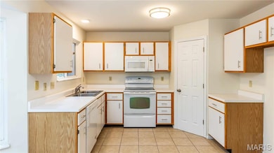 Kitchen with white appliances, light countertops, light tile patterned floors, white cabinetry, and brown cabinets