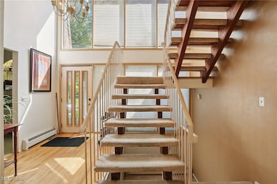 Staircase featuring baseboard heating, wood finished floors, a towering ceiling, and a chandelier