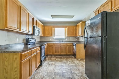 Kitchen featuring black appliances, stone finish flooring, washer / dryer, brown cabinetry, and dark countertops