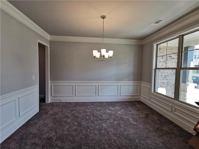 Unfurnished dining area with a decorative wall, dark colored carpet, a wainscoted wall, ornamental molding, and a chandelier