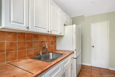 Kitchen with light tile patterned floors, white cabinets, freestanding refrigerator, tile counters, and backsplash