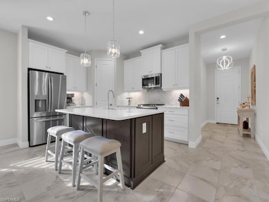 Kitchen with a chandelier, appliances with stainless steel finishes, white cabinetry, backsplash, and a breakfast bar
