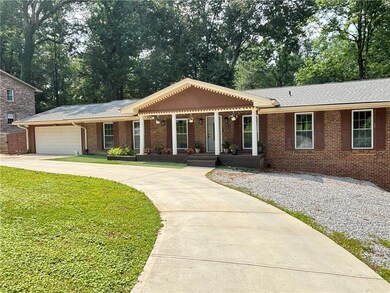 Ranch-style home with covered porch, a front yard, concrete driveway, a garage, and brick siding