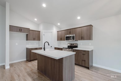 Kitchen with light countertops, appliances with stainless steel finishes, a center island with sink, light wood-type flooring, and vaulted ceiling