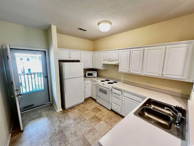 Kitchen featuring white appliances, under cabinet range hood, white cabinetry, light countertops, and a textured ceiling