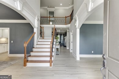 Entrance foyer with ornamental molding, arched walkways, light wood finished floors, stairway, and a high ceiling