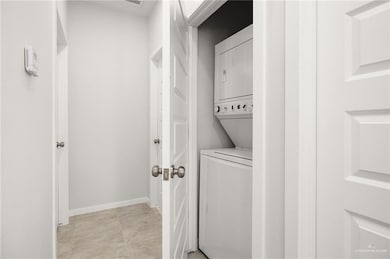 Laundry area with stacked washer / dryer and light tile patterned flooring