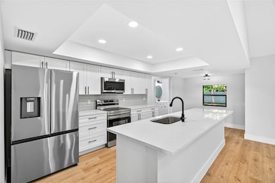 Kitchen with appliances with stainless steel finishes, a tray ceiling, white cabinets, decorative backsplash, and recessed lighting