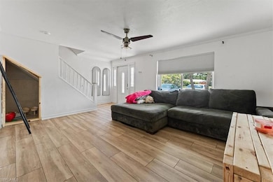Living room with light wood-style flooring, stairs, ceiling fan, and crown molding