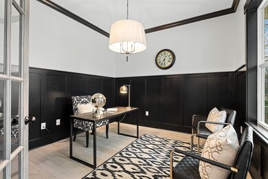 French doors off the foyer lead right into the elegant home office space, with bright white walls and contrasting black wainscoting and trim. There is plenty of light in this room from the two large windows and designer chandelier.