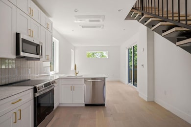 Kitchen with a peninsula, a sink, stainless steel appliances, light wood finished floors, and backsplash