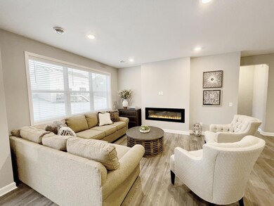The home is covered in natural light and the hard surface flooring (LVP) is continued in the family room. The focal point of the family room is the centered electric fireplace. Photo of similar home, colors and finishes will vary.