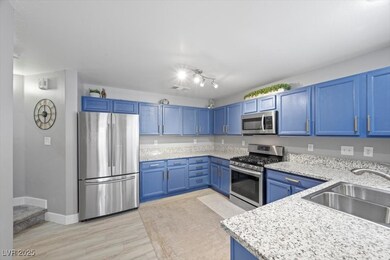 Kitchen featuring stainless steel appliances, blue cabinets, light stone countertops, and light wood-type flooring
