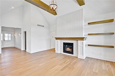 Unfurnished living room with high vaulted ceiling, visible vents, baseboards, light wood-style floors, and a notable chandelier