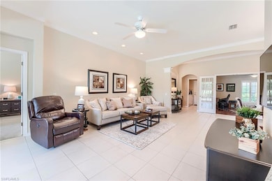 Living area with ceiling fan, arched walkways, ornamental molding, light tile patterned flooring, and recessed lighting