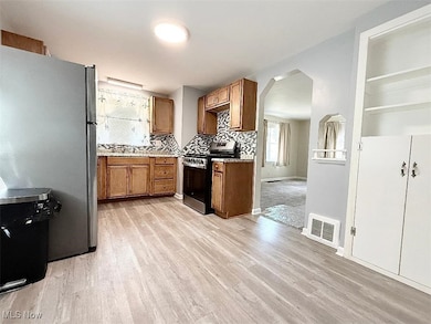 Kitchen with arched walkways, stainless steel appliances, tasteful backsplash, brown cabinetry, and laminate wood finished floors