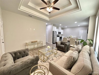 Living area with wood finished floors, a ceiling fan, a raised ceiling, and recessed lighting