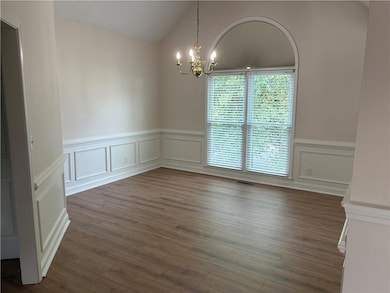 Spare room with a chandelier, vaulted ceiling, wainscoting, dark wood-style floors, and a decorative wall