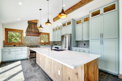 Kitchen featuring backsplash, glass insert cabinets, a kitchen island with sink, decorative light fixtures, and recessed lighting